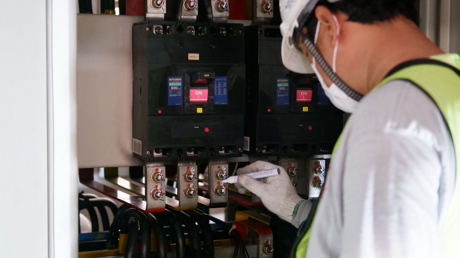 ヘルメットをかぶった作業員が分電盤の内部を点検している